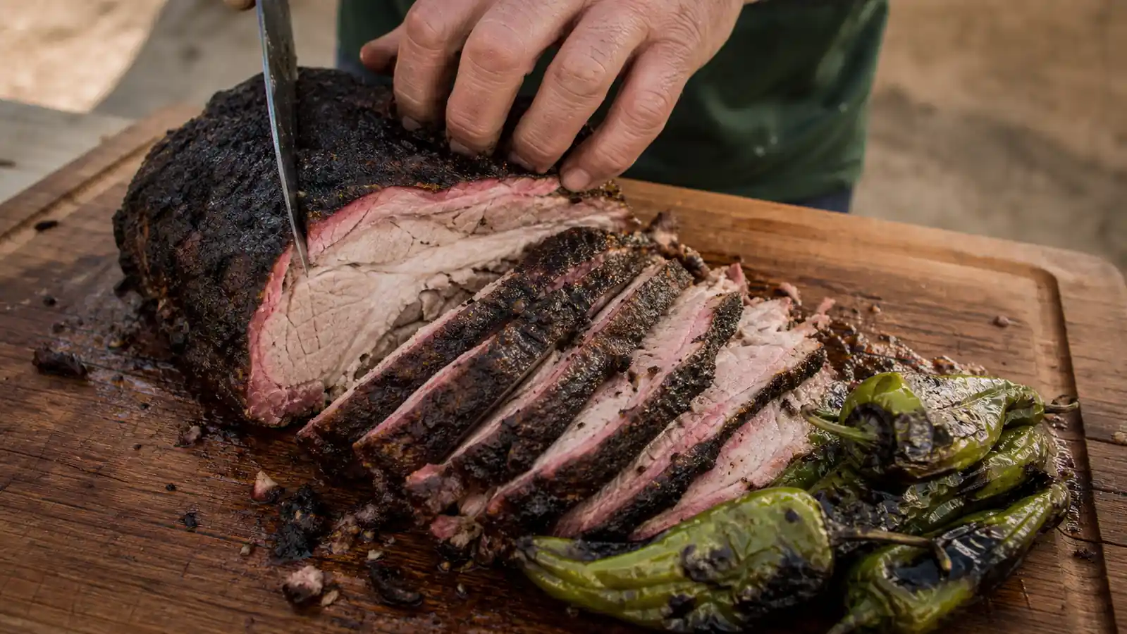 Sliced pork shoulder on a wooden cutting board showing a visible pink smoke ring under the bark