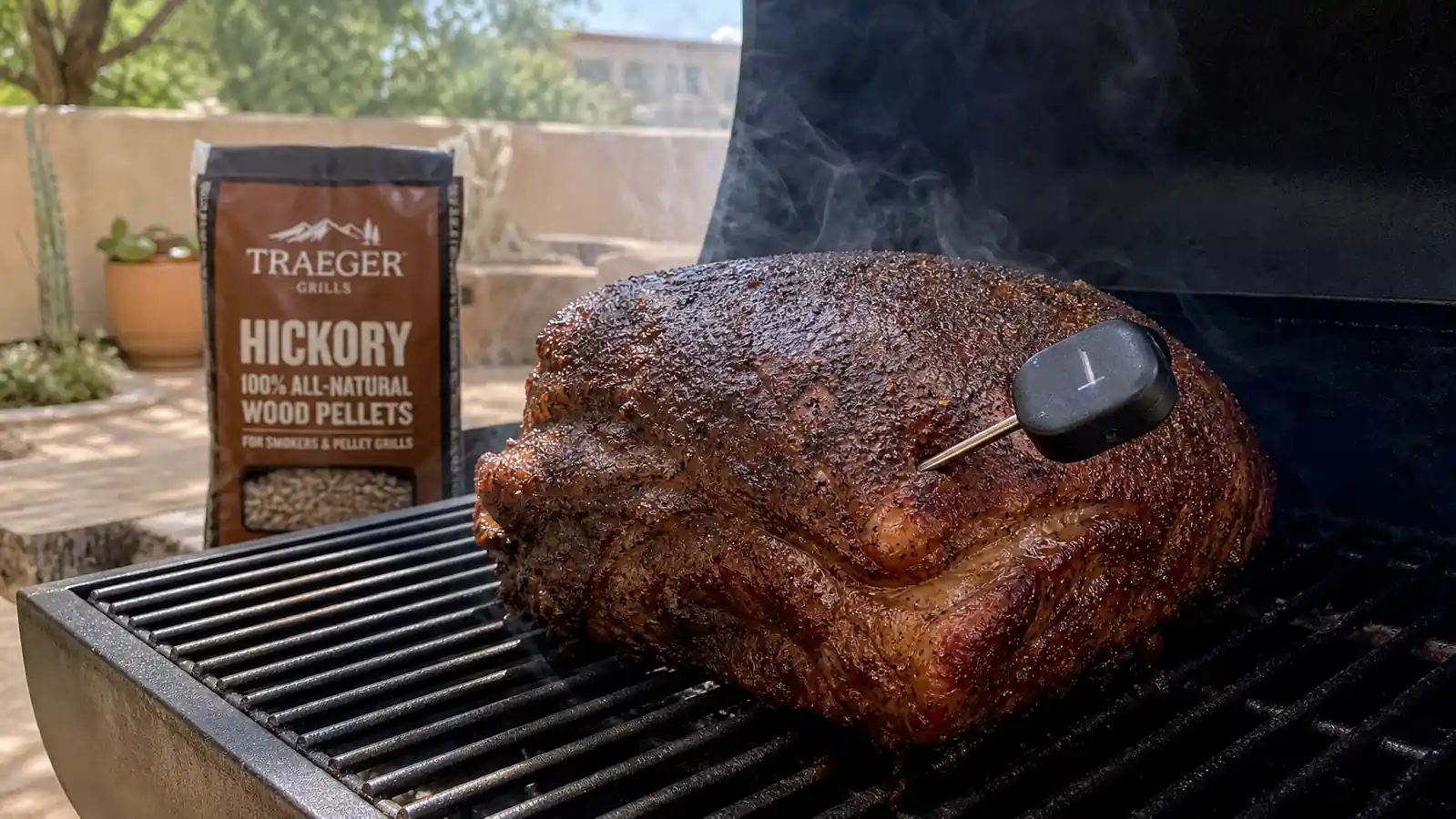 A meat thermometer probe inserted into a pork shoulder on a pellet grill grate