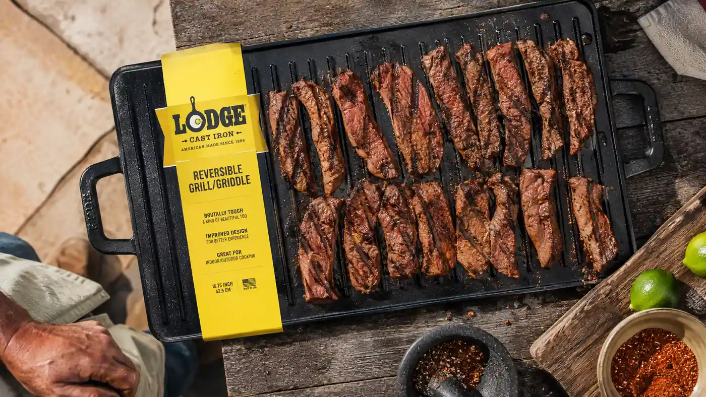 Overhead view of the ridged side of a cast iron griddle searing strips of skirt steak with distinct grill marks forming
