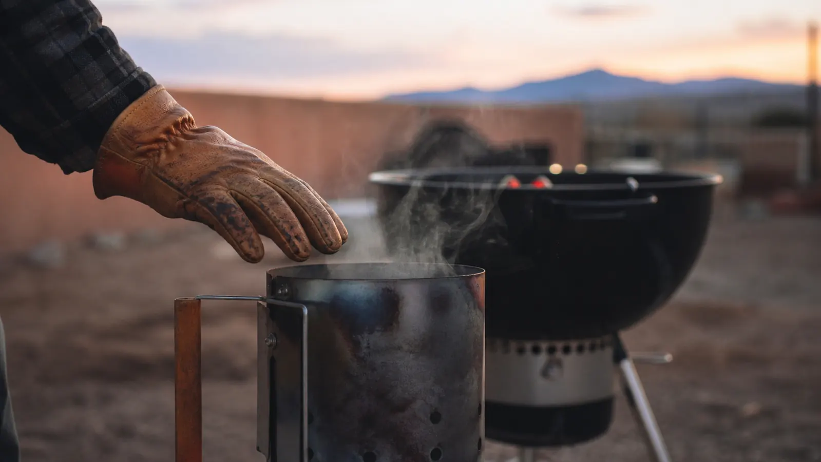 Close-up of a gloved hand testing the wood handle of a chimney starter for heat right after dumping a load of coals