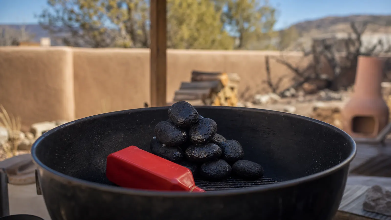 A red squeeze bottle of lighter fluid soaking a pile of charcoal briquettes in an open kettle grill