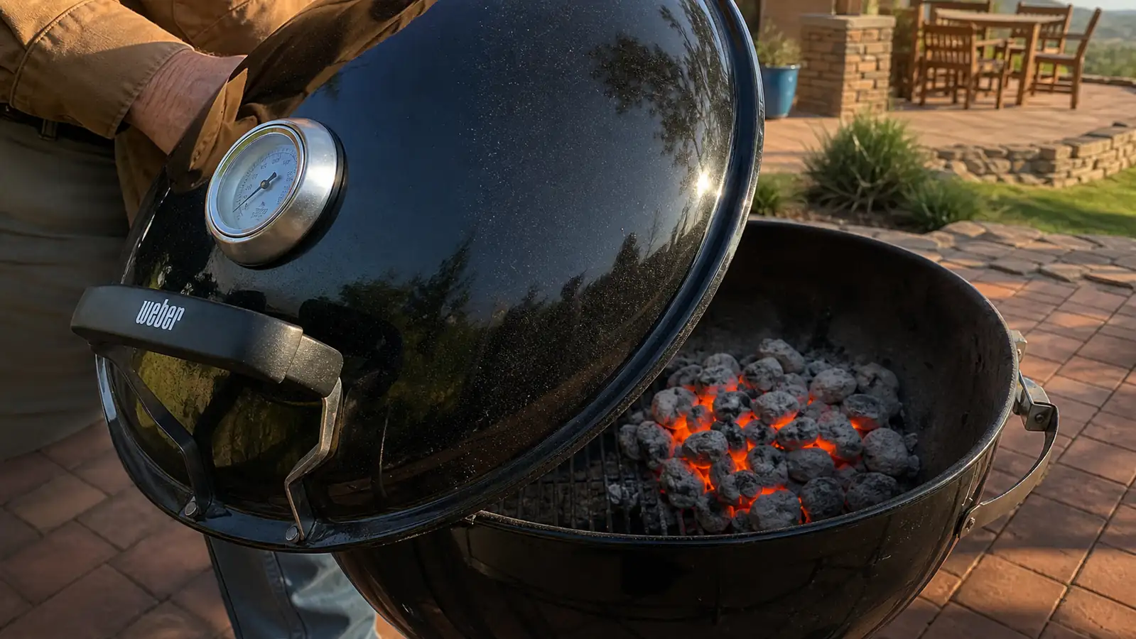 Close view of a domed grill lid thermometer positioned off to one side above a bed of glowing coals banked to the opposite side